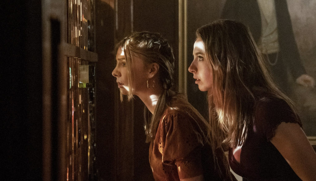 Two teen girls peek through a blind.