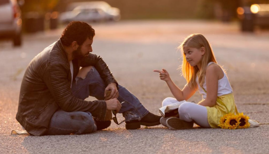 A man and a girl sit in the street and talk.