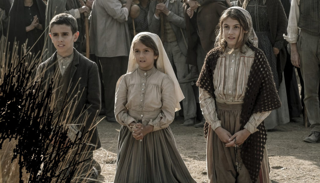 Three children stand in a field surrounded by others.