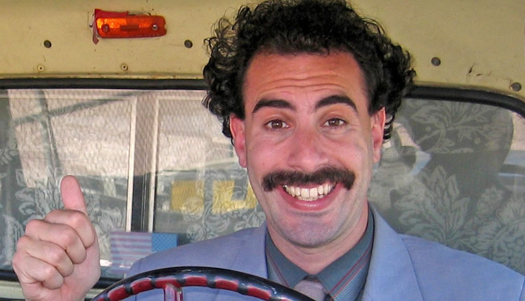 Borat (Sasha Baron Cohen) gives a thumb's up while driving.