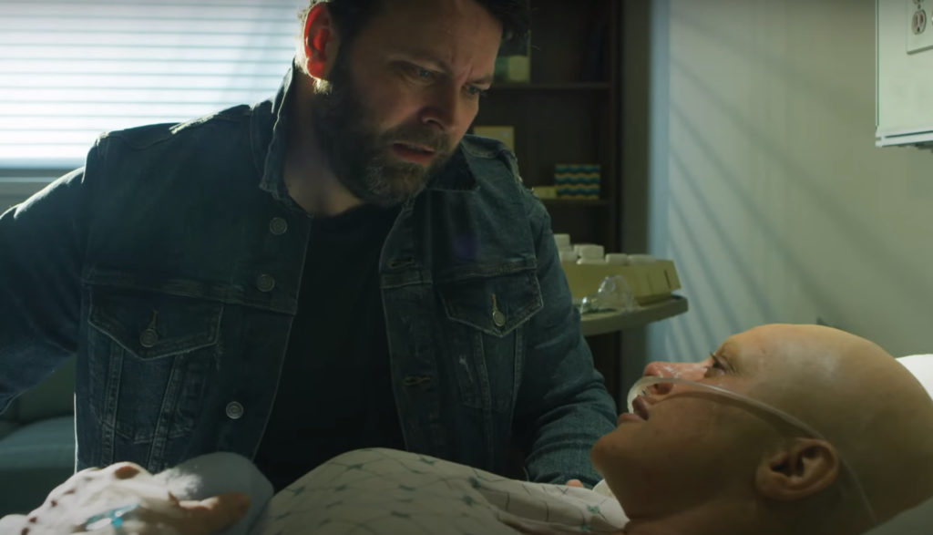 A man looks at a woman with cancer in a hospital bed.