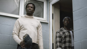 An African husband and wife stand at the front door to their home.