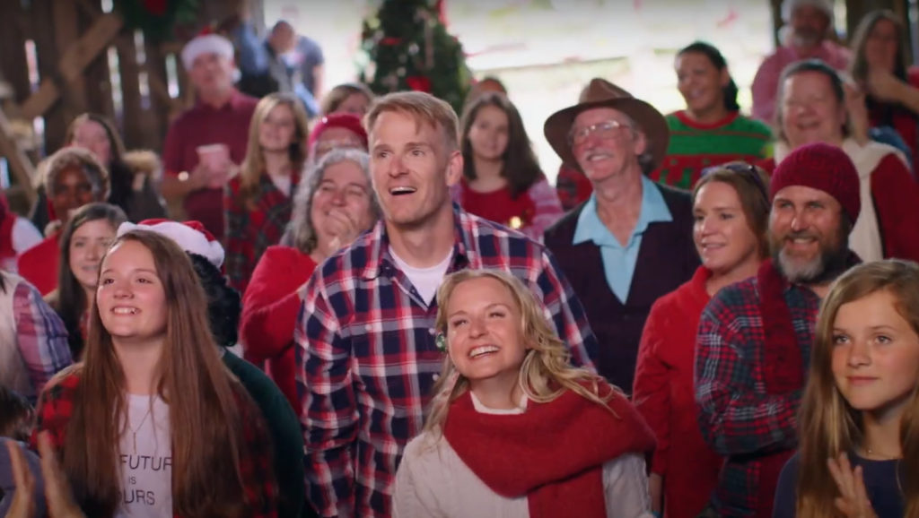 A bunch of folks smile and laugh at a Christmas event in a barn.