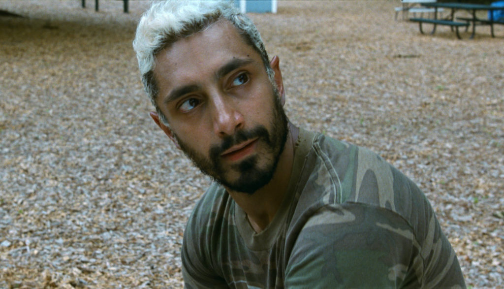 A man in a camo shirt with short died-white hair looks over his shoulder.