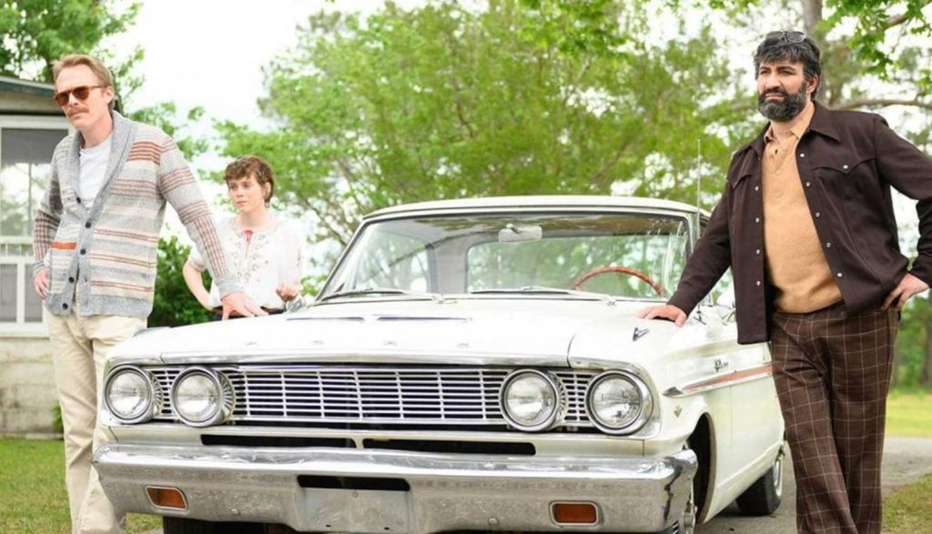 Two men and a young woman get out of a 1960s-era car.