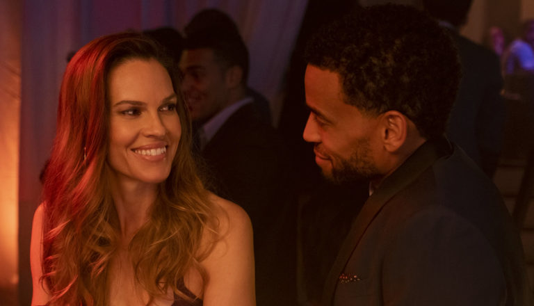 A man and a woman share a drink and smile at a bar.