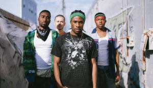 A group of four men in the city walk toward the camera.