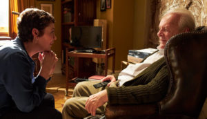 An elderly man sits in a chair and talks to his middle-aged daughter.