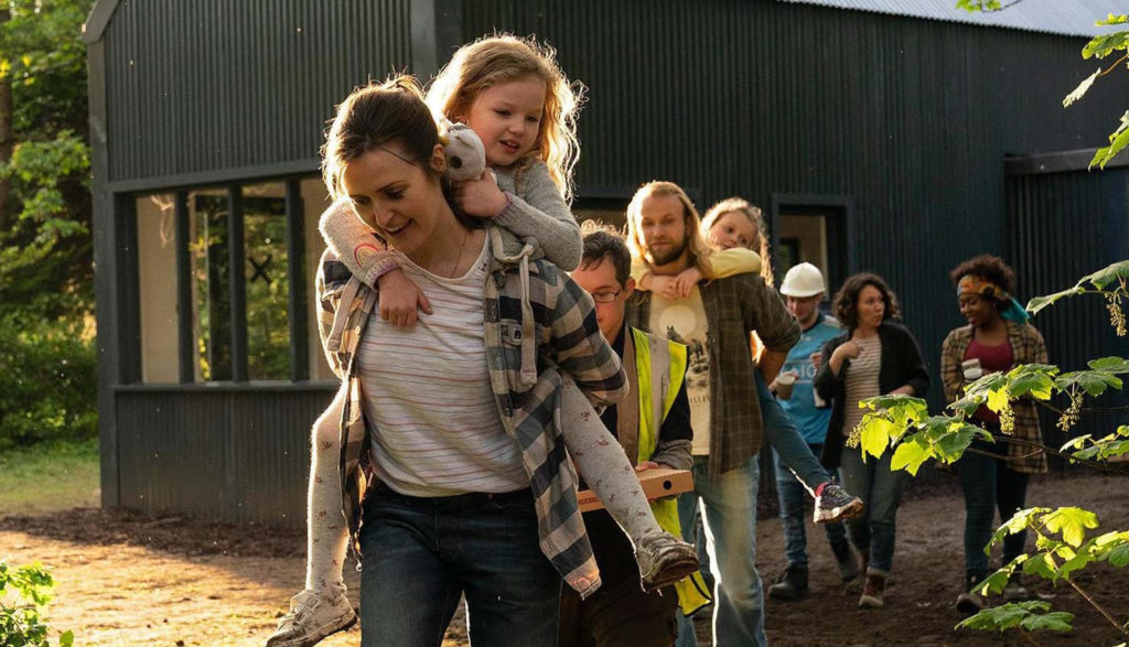 A woman walks away from a construction project with her daughter on her back and other volunteers walking behind her.