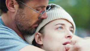A man embraces a woman who stares upward sadly.