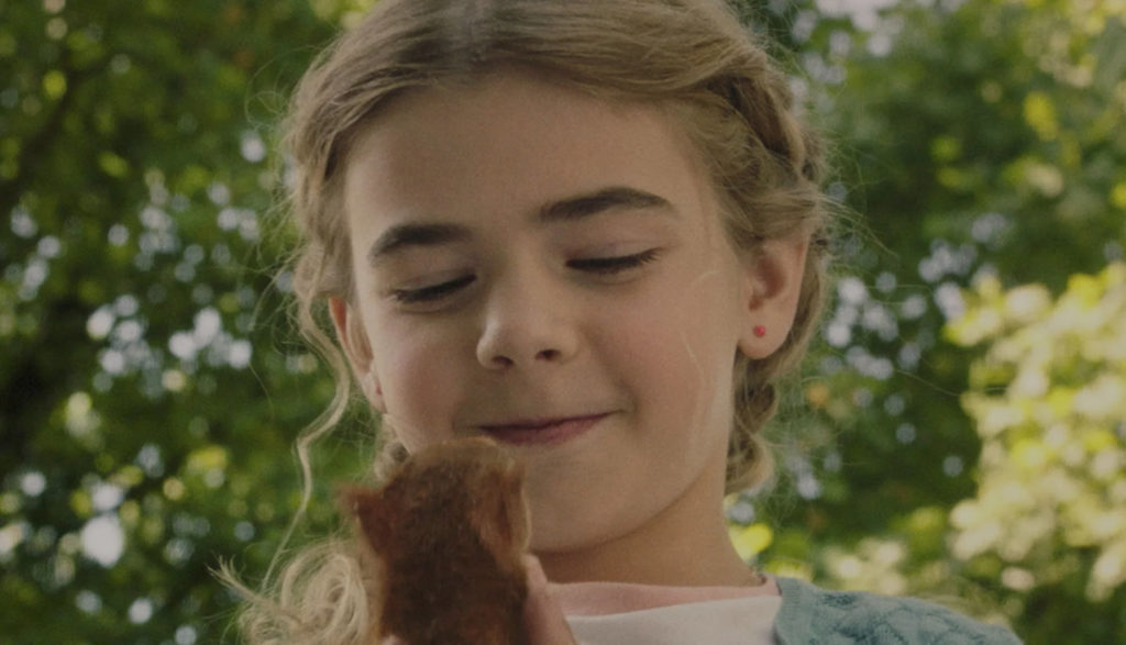 A young girl holds and smiles at a squirrel in her hands.