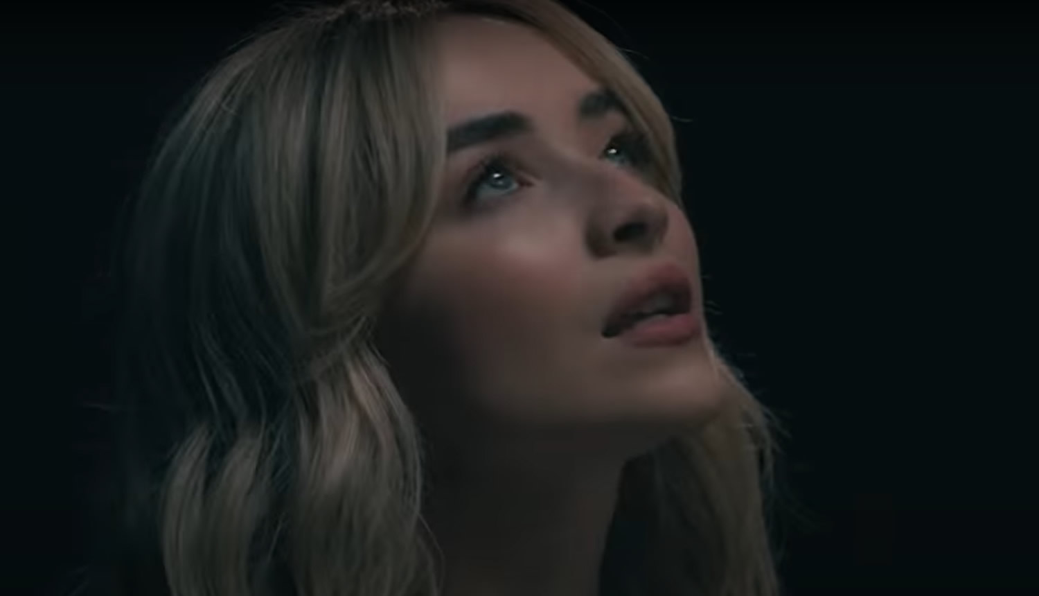 Singer Sabrina Carpenter looks up against a black backdrop. 