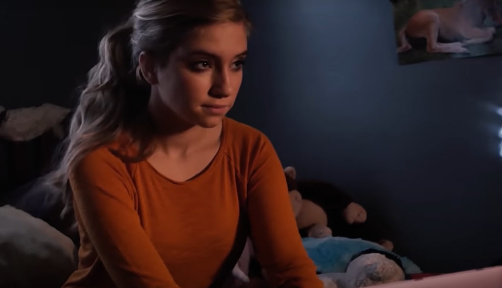 A teen sits at her computer, looking up from the screen.