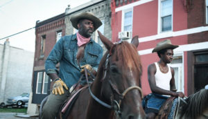 A man and a young man ride horses through a town.