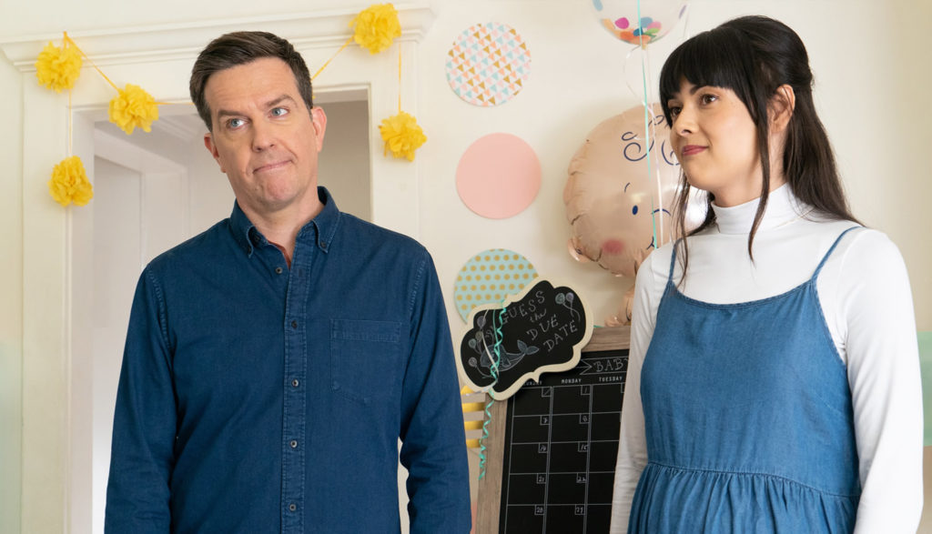 An older man and a pregnant young woman stand in a nursery with baby stuff around them.