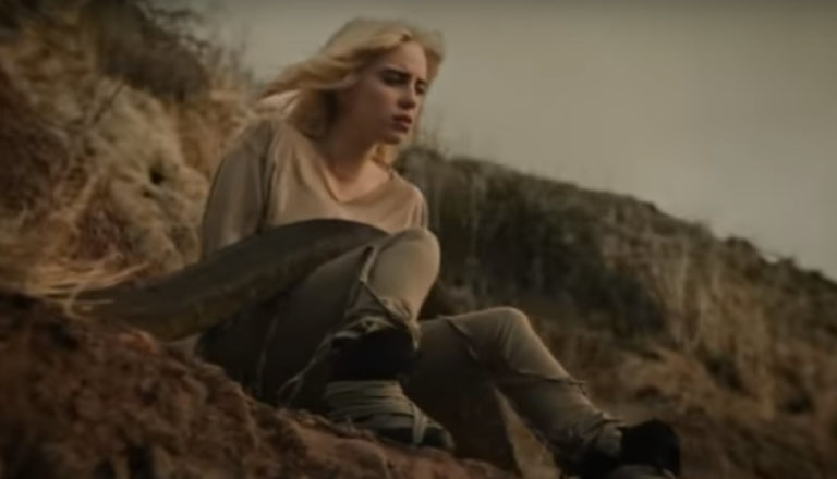 Singer Billie Eilish sits on a cliff as a python slides over her in the video for her song "Your Power."