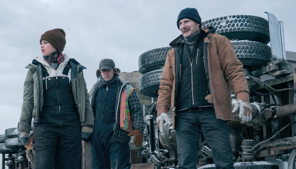 Liam Neeson and friends are warmly dressed and standing by a tipped over truck in the Artic thriller "The Ice Road."