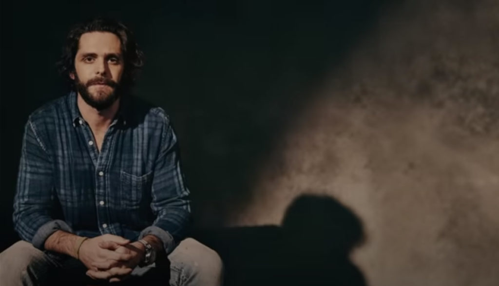 Portrait pose of country singer Thomas Rhett sitting in a dark room.