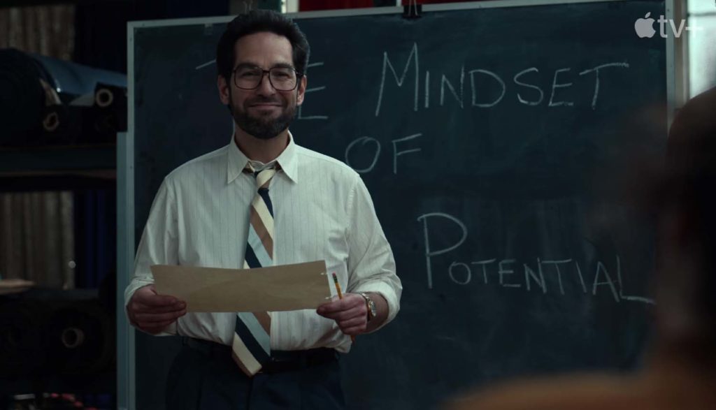 Man smiling in front of chalkboard from The Shrink Next Door tv show