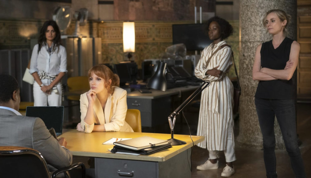 Four female spies talk to a handler in an office.