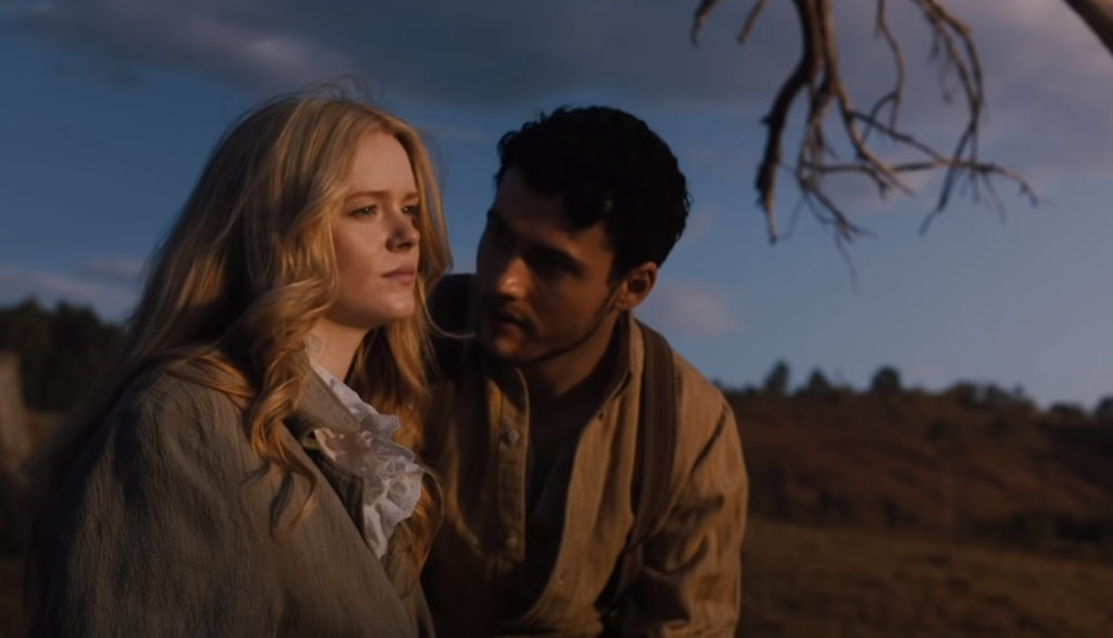 A man and a woman sit close, talking, on a hillside.