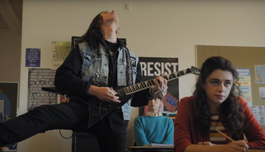 A teen guitar player with long hair rocks out in class while a female student makes a disdainful face.