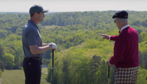 Two men stand, talking, on a golf course.