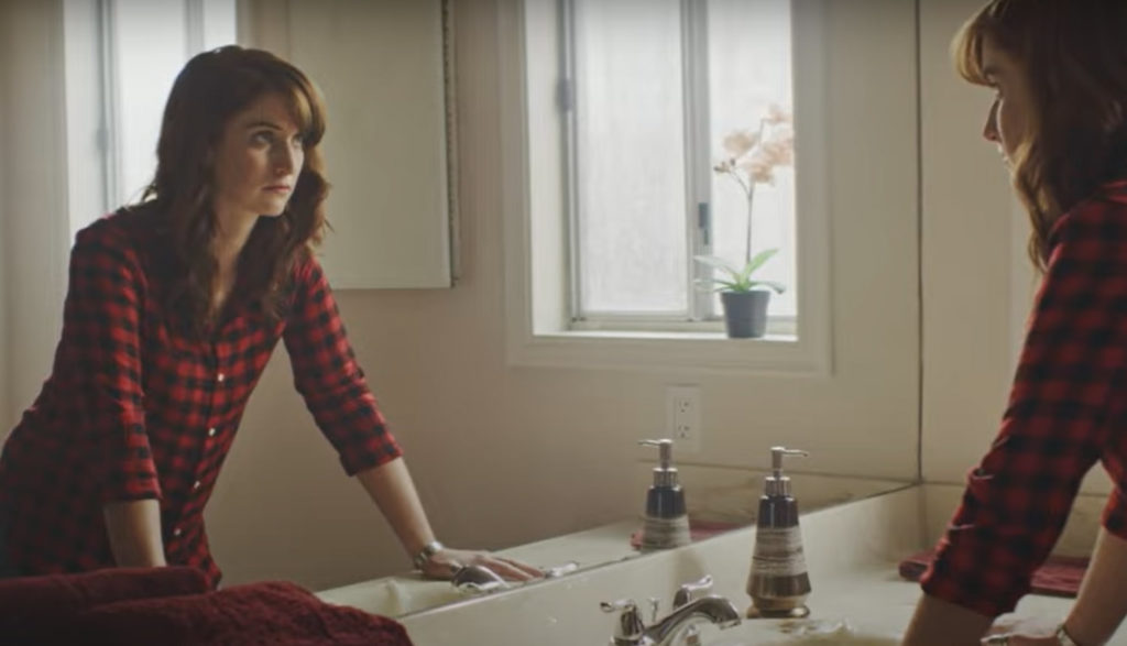 A woman, likely considering abortion, stares at her image pensively in the mirror.