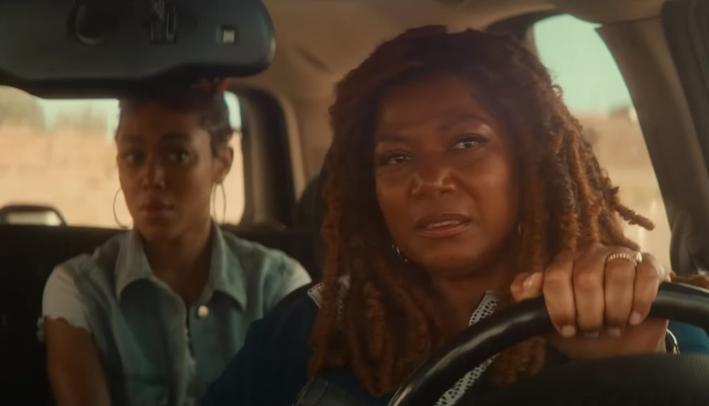 A woman drives with a concerned look on her face as she looks in the rearview mirror.