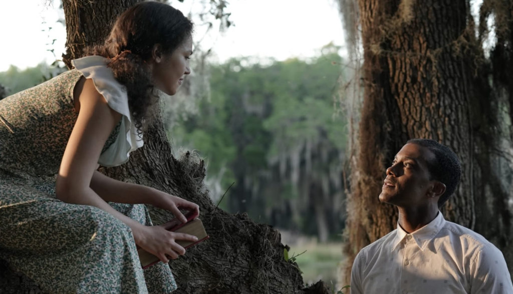 A man looks up at a woman as he talks to her while she sits on a tree limb.