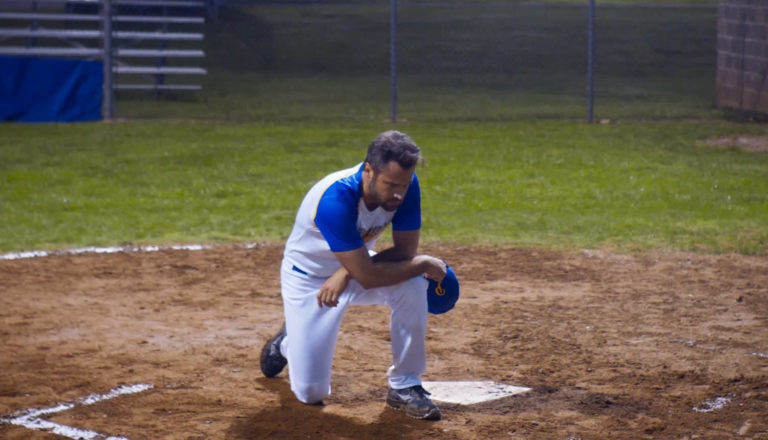 A baseball coach kneels and prays at home plate.