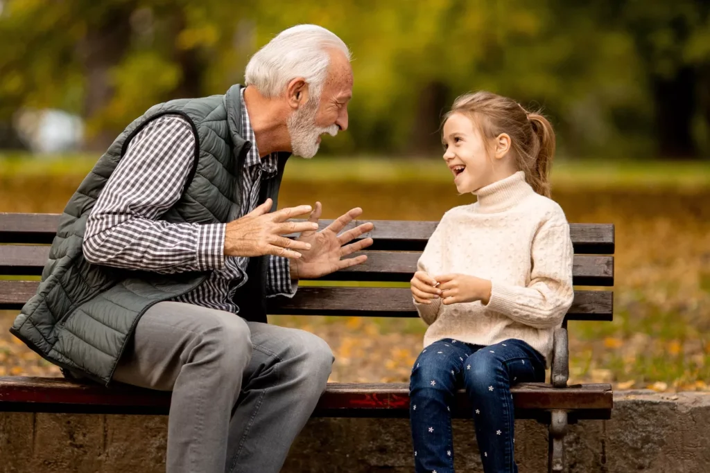 Grandparents and screen time — grandfather and granddaughter laughing together on a park bench