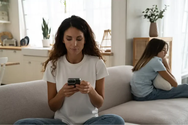 Mother focused on her phone while daughter sits upset beside her