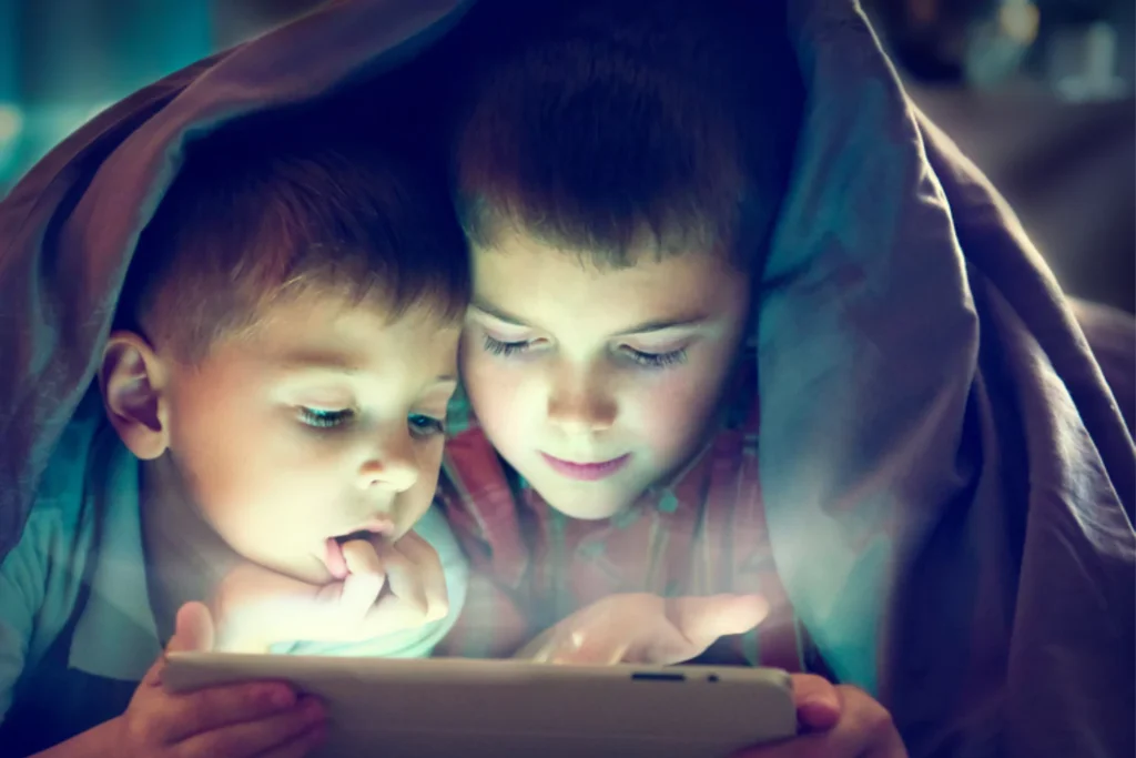 Two young brothers snuggling under a blanket while watching something on a tablet together