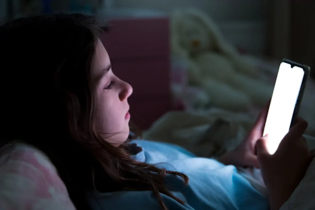 young teen laying dow in the dark looking at her phone|young teen laying dow in the dark looking at her phone