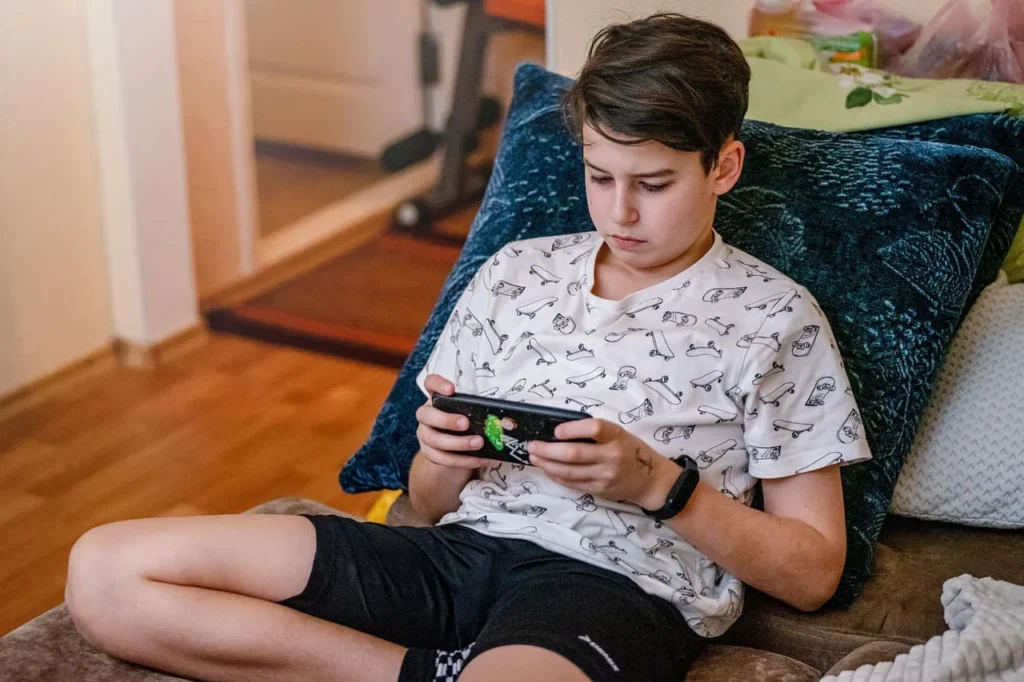 Teen boy reclining on a couch and playing a game on his phone
